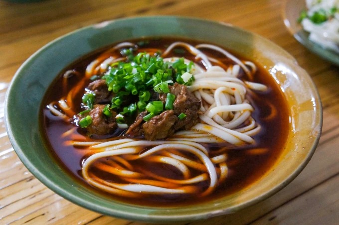 Cuenco de fideos con caldo oscuro, carne y verduras picadas