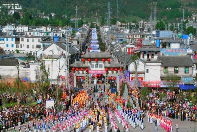 Ein großer Festzug füllt eine Straße zwischen traditionellen Gebäuden in Dali