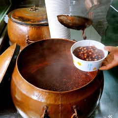 Sweet porridge being ladled beside a large copper pot